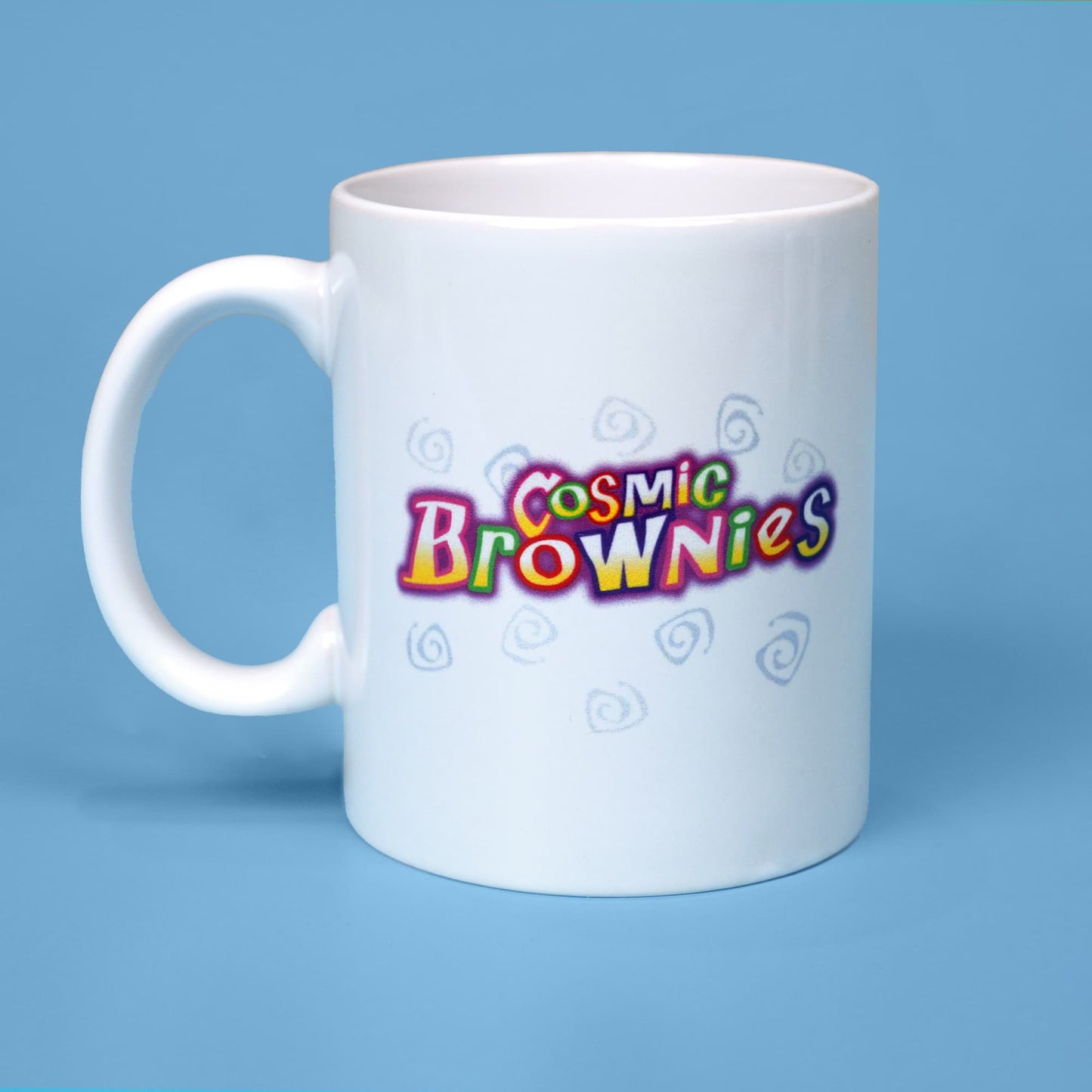 White ceramic mug with a colorful 'Cosmic Brownies' logo from Little Debbie, featuring stylized text in pink, yellow, green, and white. The design includes playful, light blue swirl patterns surrounding the logo. The mug is set against a soft blue background.
