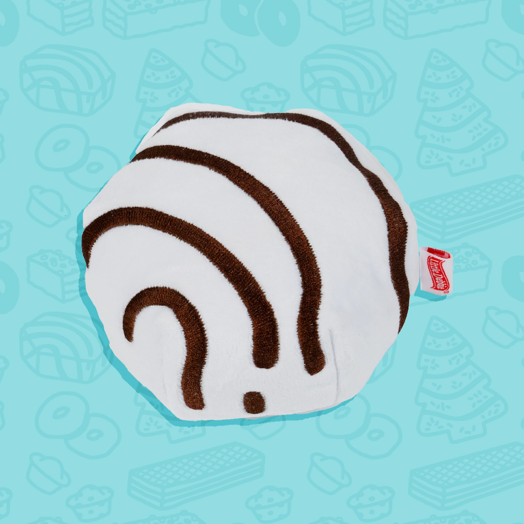 
A Little Debbie Zebra Cake dog toy shaped like the classic Zebra Cake snack. The toy is round with a white base, featuring the signature curved brown zebra-like stripes. A small red Little Debbie logo tag is attached to the side. The background is light blue with faint outlines of various Little Debbie snacks