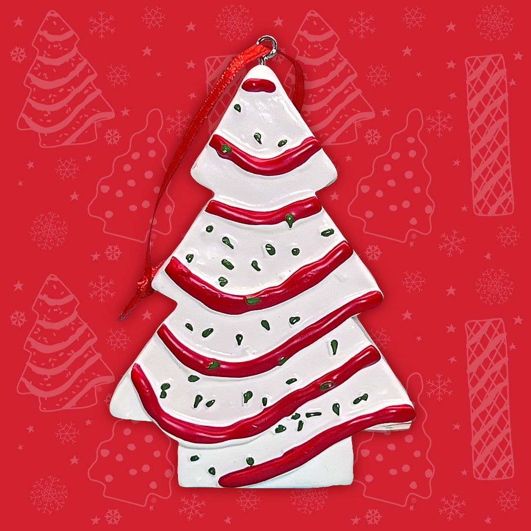 A Little Debbie Christmas Tree Cake ornament, decorated with white frosting, red stripes, and green sprinkles, against a vibrant red background with faint snowflakes and Christmas Tree Cake and Brownie outlines.