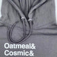 Close-up view of the top part of a Little Debbie Fan Favorites gray hoodie. The fabric displays a finely knit texture, and the drawstrings are braided with metal aglets. Just below the drawstrings, white text reads 'Oatmeal& Cosmic&'. 