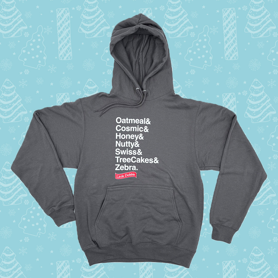Gray hoodie displayed on a white background with the hood up. The front of the hoodie features a list of product names in white text, each separated by an ampersand: 'Oatmeal& Cosmic& Honey& Nutty& Swiss& TreeCakes& Zebra.' In the bottom corner, there's a small red logo with the text 'Little Debbie'. It's set against a light blue background patterned with white illustrations of Christmas Trees Cakes, Christmas Tree Brownies, snowflakes, and other winter motifs.