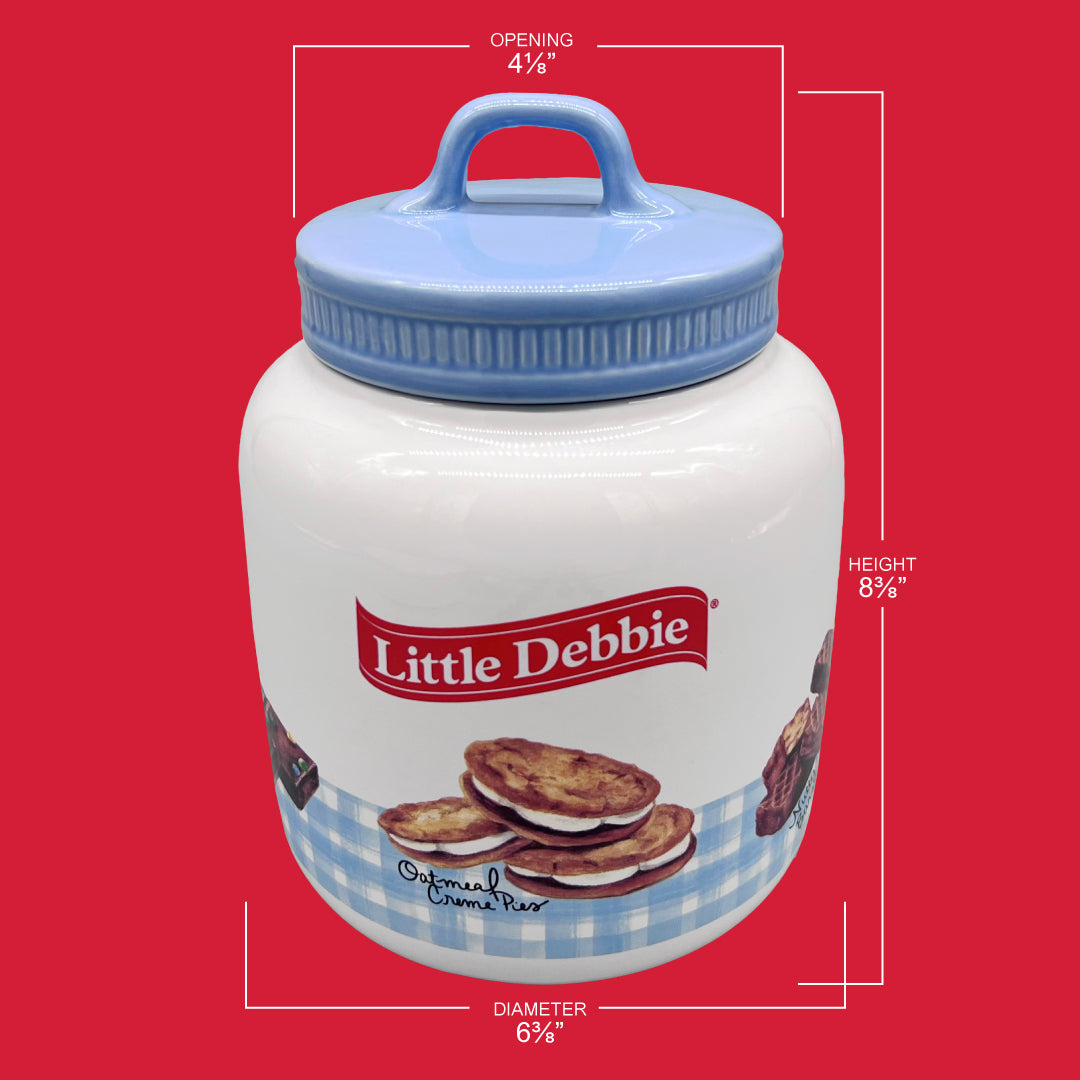 This image showcases a Little Debbie collectible cookie jar with dimensions labeled. The jar has a height of 8⅜ inches, a width of 6⅜ inches, and an opening of 4⅛ inches. It's adorned with a blue gingham pattern at the bottom and has an image of Oatmeal Creme Pies. The jar features a blue lid with a loop handle. The Little Debbie logo is prominently displayed in red above the cookie depiction. The jar is set against a contrasting red background.