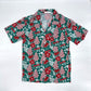Front view of the Green Little Debbie Hawaiian button up shirt, showcasing a design of red and white Little Debbie Christmas Tree Cakes, Red Ribbon Logos, and an aloha pattern of leaves and flowers.