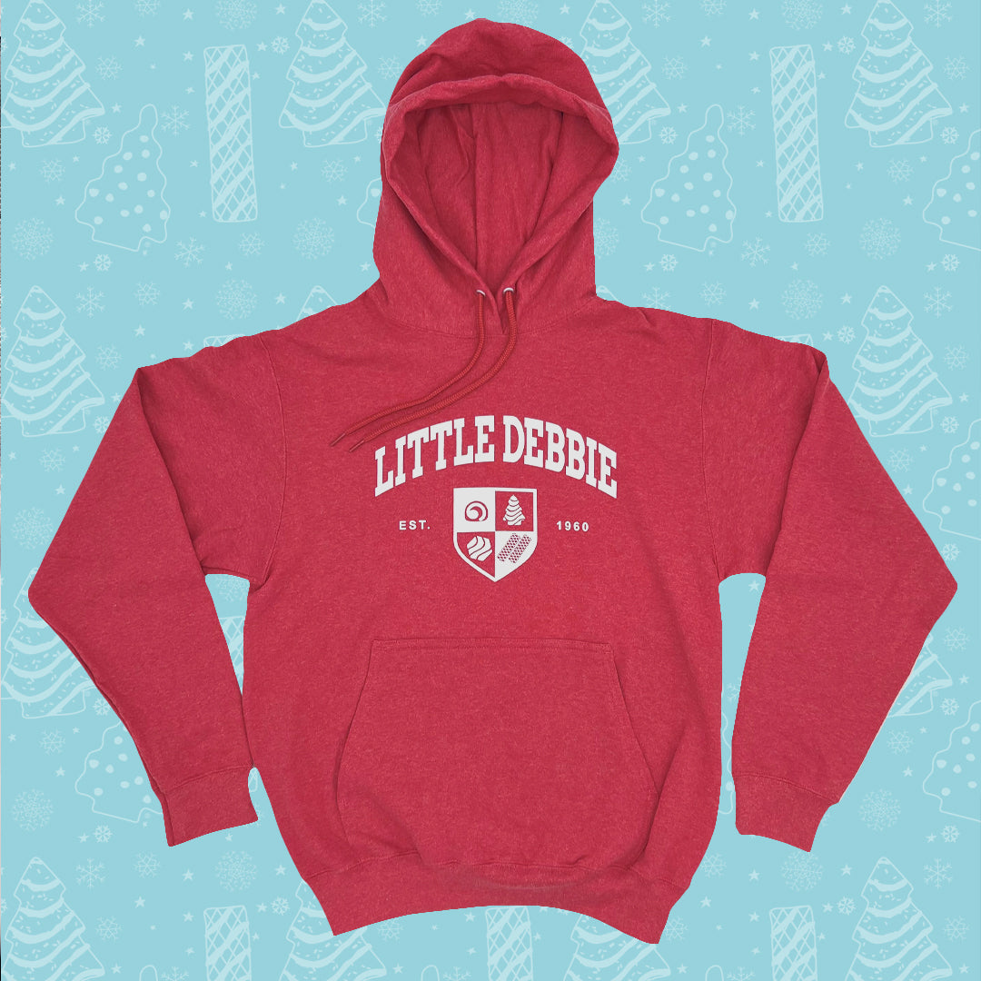 Little Debbie University Red hoodie with the words 'LITTLE DEBBIE' printed in white on the front, accompanied by a shield emblem containing various symbols and the text 'EST. 1960'. The hoodie has a front pocket and a hood with drawstrings. It's set against a light blue background patterned with white illustrations of Christmas Trees Cakes, Christmas Tree Brownies, snowflakes, and other winter motifs.