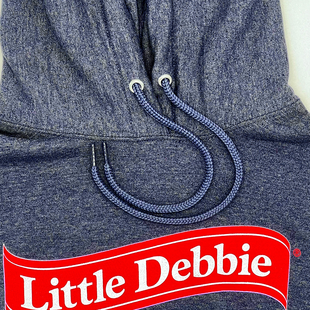 Close-up of a blue Little Debbie Unwrap a smile hoodie, featuring a blue drawstring with metal eyelets. A Little Debbie red ribbon logo in bold red and white lettering is prominently displayed at the bottom of the image.