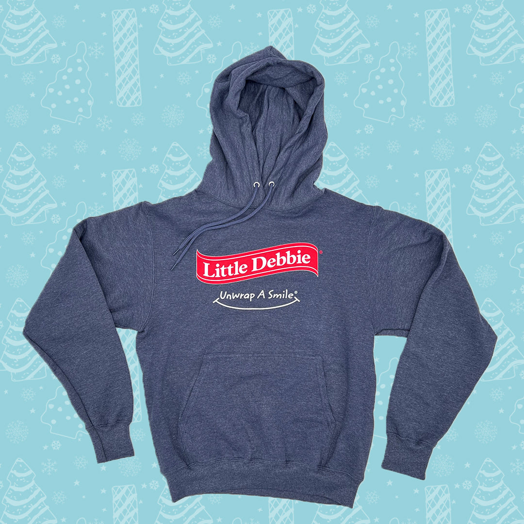 Blue Little Debbie Unwrap a Smile hoodie with a prominent 'Little Debbie' logo in red and white on the front, accompanied by the slogan 'Unwrap A Smile' underneath. It's set against a light blue background patterned with white illustrations of Christmas Trees Cakes, Christmas Tree Brownies, snowflakes, and other winter motifs..