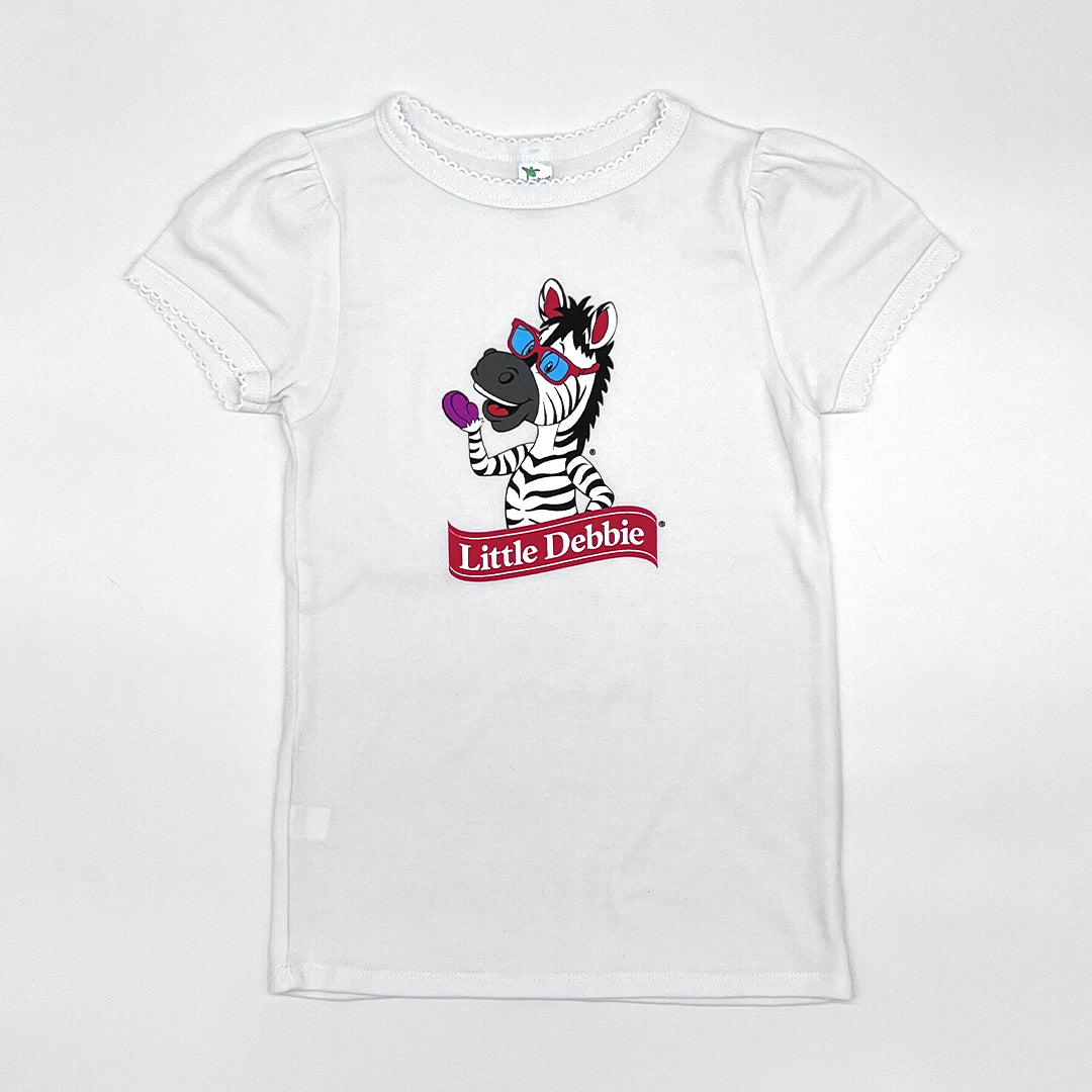 Front view of a white Little Debbie toddler shirt featuring Zain the Zebra™ waving. The sand sleeves.hirt also showcases a scalloped detail on the neck 
