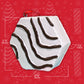 Close-up view of the Little Debbie Zebra Cake ornament with measurements indicating a height of 2 5/8 inches, width of 2 5/8 inches, and thickness of 1 1/8 inch. The ornament, featuring the cake's signature white icing with stripes, is attached to a red ribbon, against a festive red background with white holiday motifs.