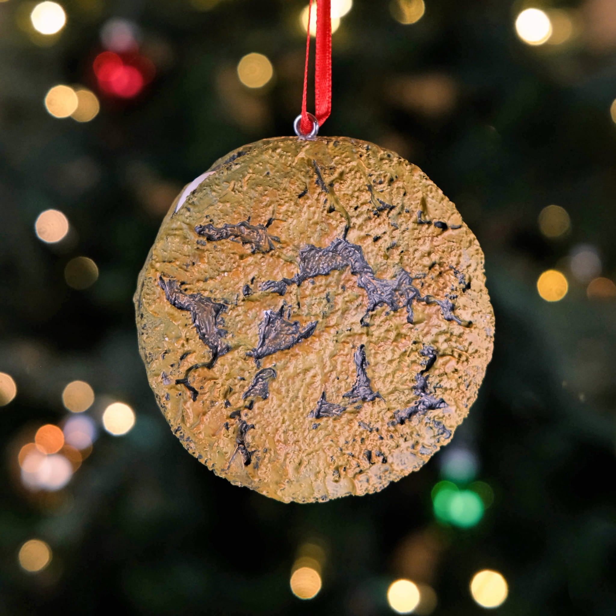 Little Debbie Oatmeal Creme Pie Ornament featuring a textured cookie design, hanging by a red ribbon in front of a softly lit Christmas tree.