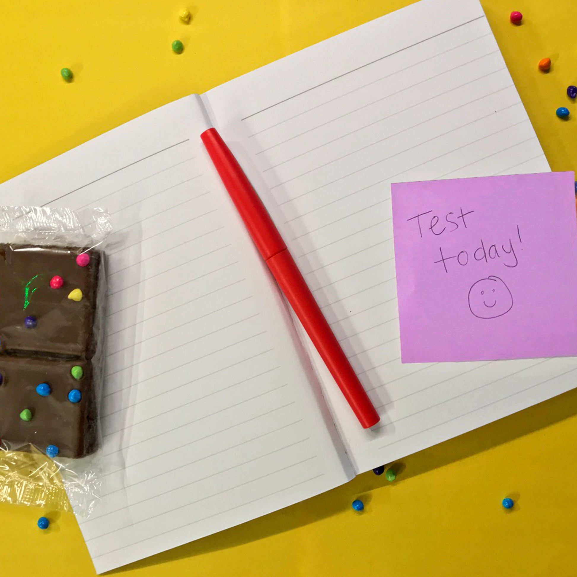 Little Debbie® Cosmic® Brownies Journal open on yellow background with a sticky note, a red pen and a Cosmic® Brownie on lined paper.